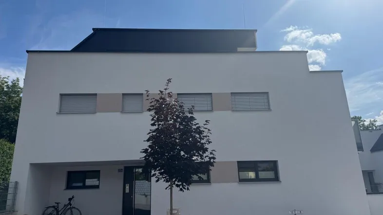 Moderne weiße Fassade eines Wohngebäudes mit klaren Linien und Flachdach unter blauem Himmel.