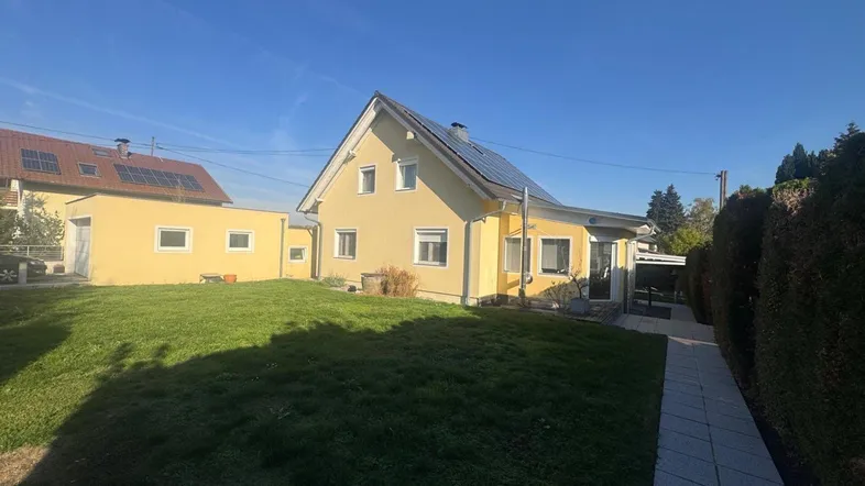 Gelbes Einfamilienhaus mit grünem Rasen, Photovoltaikanlage auf dem Dach und gepflegtem Garten.