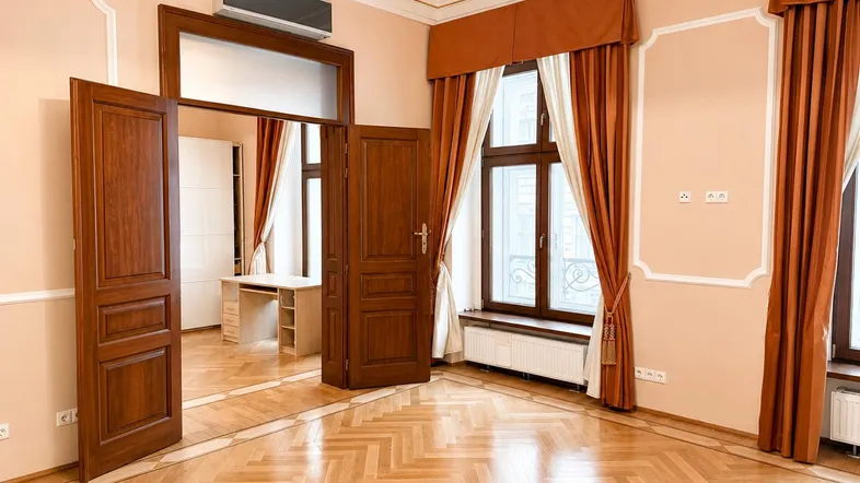 Helles Wohnzimmer mit Fischgrätparkett, hohen Decken und eleganten Vorhängen.