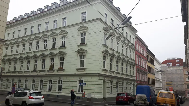 Historisches Eckgebäude mit klassischer Fassade und vielen Fenstern in einer städtischen Umgebung.