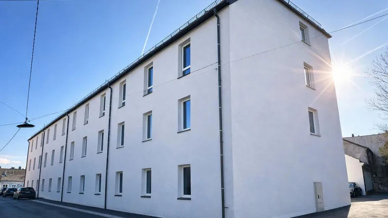 Moderne weiße Fassade eines Mehrfamilienhauses unter blauem Himmel mit Sonnenschein.