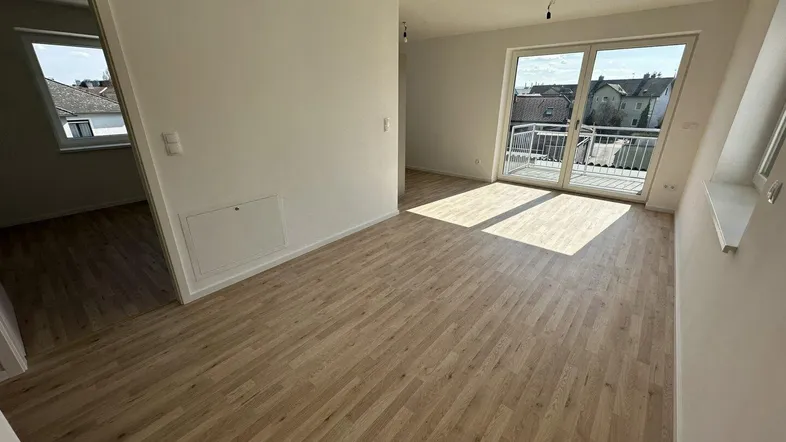 Heller Wohnbereich mit Parkettboden und Zugang zu einem Balkon, durchflutet von Tageslicht.