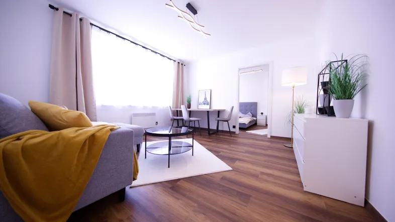 Helles Wohnzimmer mit Holzboden, Sofa, Essbereich und großem Fenster, modern eingerichtet.