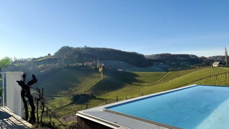 Infinity-Pool und Holzterrasse mit weitem Blick über die malerischen Weinberge und die grüne Hügellandschaft.