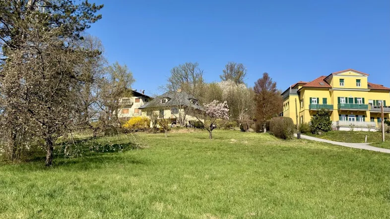 Weitläufige Grünfläche mit Blick auf mehrere Gebäude und die umliegende Landschaft unter blauem Himmel.