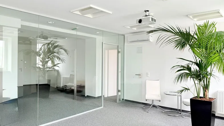 Modernes Büro mit Glaswänden, Teppichboden und einem Deckenprojektor für Präsentationen.
