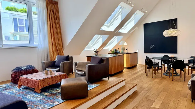 Geräumiger Wohn- und Essbereich mit Holzboden, großen Fenstern und Dachschrägen.
