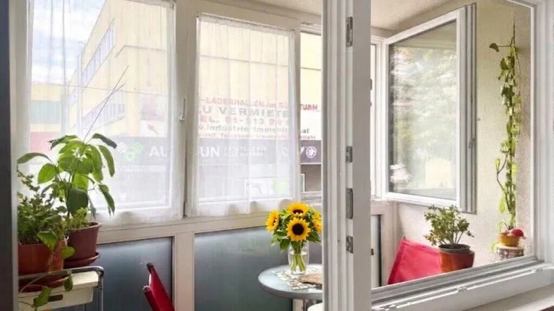 Gemütliche verglaste Loggia mit Pflanzen, kleinem Tisch und Blick auf die Stadtstraße.