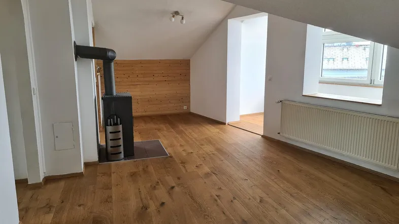 Geräumiges Wohnzimmer im Dachgeschoss mit Holzboden, Kaminofen und schrägen Wänden.