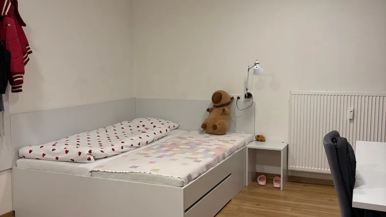 Helles Schlafzimmer mit Einzelbett, Schreibtisch und Laminatboden, ausgestattet mit einem Heizkörper.