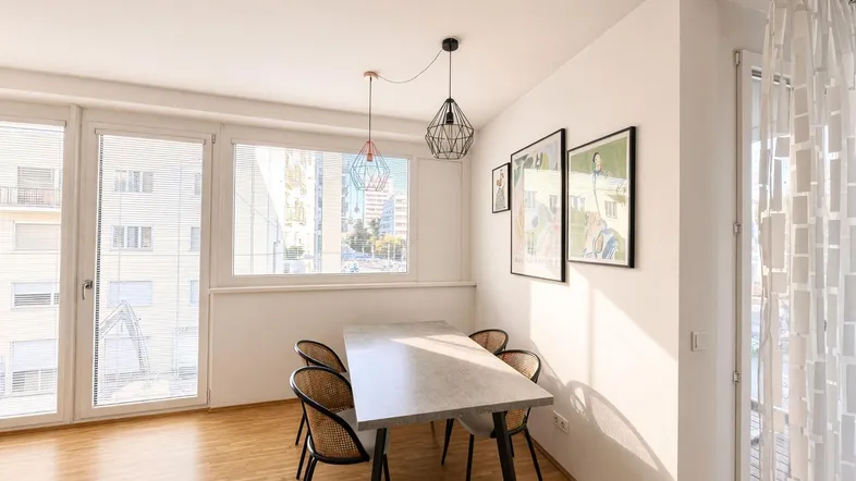 Heller Essbereich mit modernem Tisch, Stühlen und Zugang zum Balkon, umgeben von großen Fenstern.