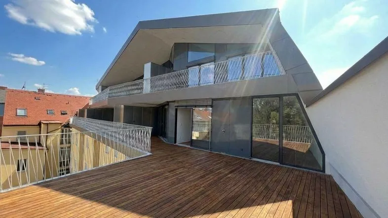 Moderne Architektur mit großer Holzterrasse und Blick auf die Stadt unter strahlendem Sonnenschein.