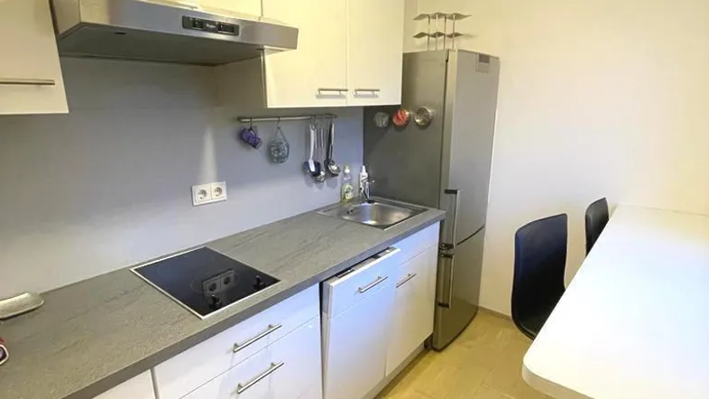 Moderne Küche mit weißen Schränken, grauer Arbeitsplatte und integrierten Geräten, inklusive Essbereich.