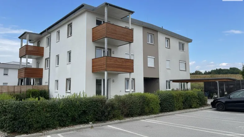 Modernes Mehrfamilienhaus mit Balkonen und Außenparkplätzen unter blauem Himmel.