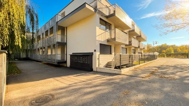 Modernes Mehrfamilienhaus mit Balkonen und gepflegter Außenanlage unter blauem Himmel.
