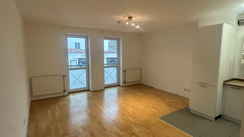 Helles Wohnzimmer mit Parkettboden und integrierter Küchenzeile, mit Zugang zu zwei französischen Balkonen.