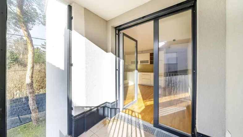 Heller Balkon mit Fliesenboden und Blick ins Grüne, verbunden mit dem Innenbereich durch große Glastüren.
