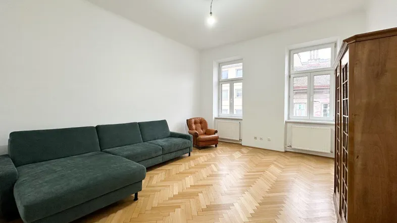 Helles Wohnzimmer mit Fischgrätparkett, einem grünen Sofa und großen Fenstern.