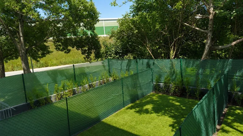 Kleiner, eingezäunter Gartenbereich mit Kunstrasen und umgebenden Bäumen, ideal für Entspannung im Freien.