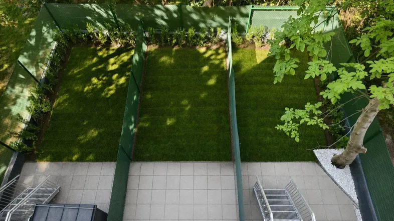 Blick von oben auf mehrere kleine, eingezäunte Gartenparzellen mit Rasenfläche und gefliestem Terrassenbereich.
