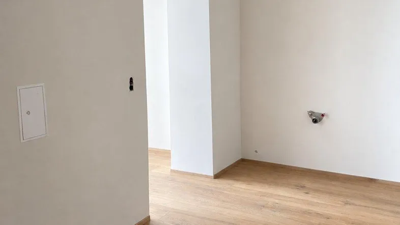 Heller Raum im Rohbau mit weißen Wänden und neu verlegtem Holzfußboden.