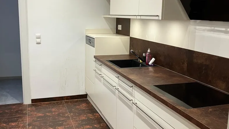 Moderne Küche mit weißen Schränken, dunkler Arbeitsplatte und braunen Fliesenboden.
