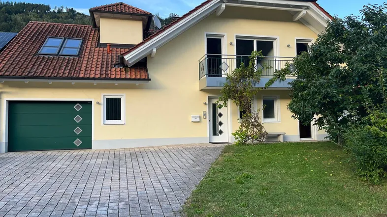 Gelbes Einfamilienhaus mit rotem Ziegeldach, Garage und gepflasterter Auffahrt.