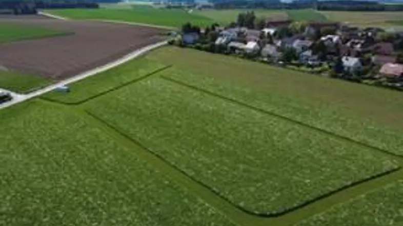 Luftaufnahme eines grünen Feldes mit angrenzendem Dorf und weitem Blick.
