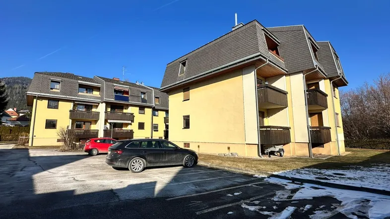 Mehrfamilienhaus mit mehreren Balkonen und einem Parkplatz im Freien an einem sonnigen Wintertag.