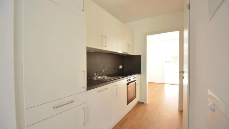 Moderne Einbauküche mit weißen Schränken, dunkler Arbeitsplatte und integrierten Geräten.