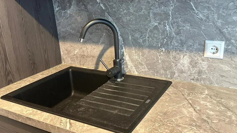 Moderne Küche mit schwarzem Spülbecken, Armatur und Arbeitsplatte in Steinoptik.