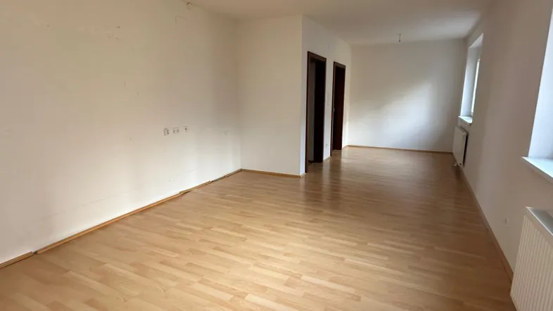 Helles, leeres Wohnzimmer mit Laminatboden und weißen Wänden, bereit zur individuellen Gestaltung.