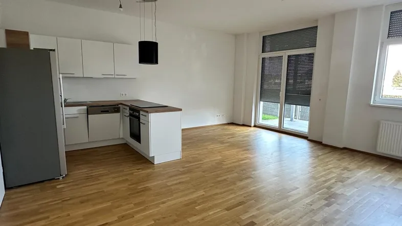 Heller offener Wohnbereich mit integrierter Küche, Parkettboden und Zugang zur Terrasse.
