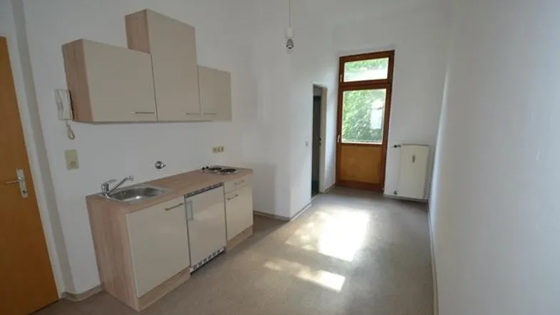 Kleine Einbauküche mit Spüle und Kochfeld in einem hellen Raum mit Zugang zum Balkon.