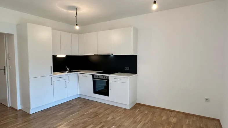 Moderne Einbauküche mit weißen Schränken, dunkler Rückwand und hellem Parkettboden in einem offenen Raum.