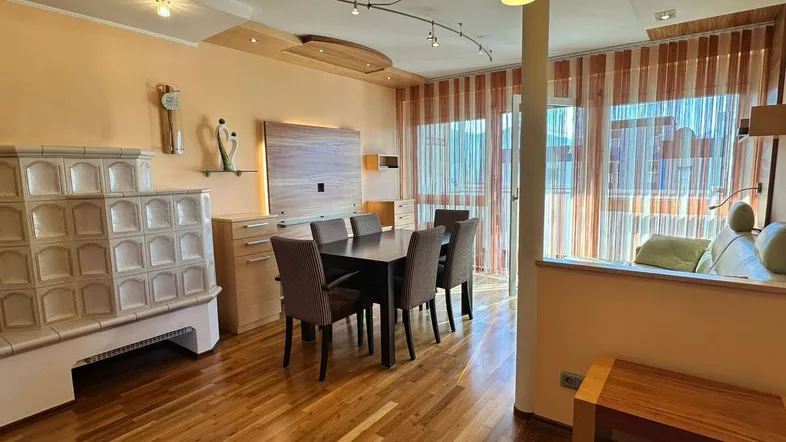 Geräumiger Wohn-Essbereich mit Holzboden, Kachelofen und Zugang zum Balkon.