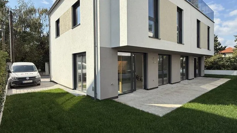 Moderne Neubau-Doppelhaushälfte mit Garten, Terrasse und Dachterrasse unter blauem Himmel.