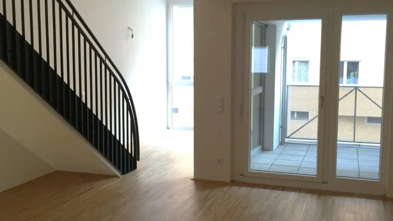Heller Wohnbereich mit moderner Treppe, Holzboden und Zugang zu einem Balkon.