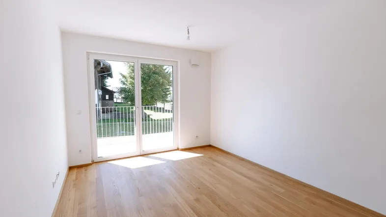 Helles Zimmer mit Holzboden und Zugang zu einem Balkon, ideal für Wohn- oder Schlafbereich.