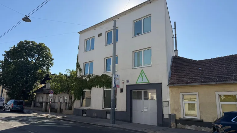 Ansicht des weißen Gebäudes von der Straße mit mehreren Fenstern und einem Garagentor.