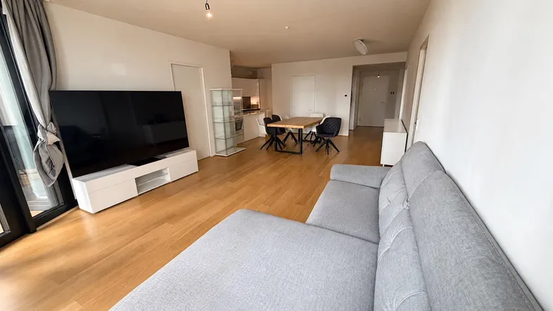 Heller offener Wohn- und Essbereich mit Holzboden, großem Fernseher und Zugang zum Balkon.