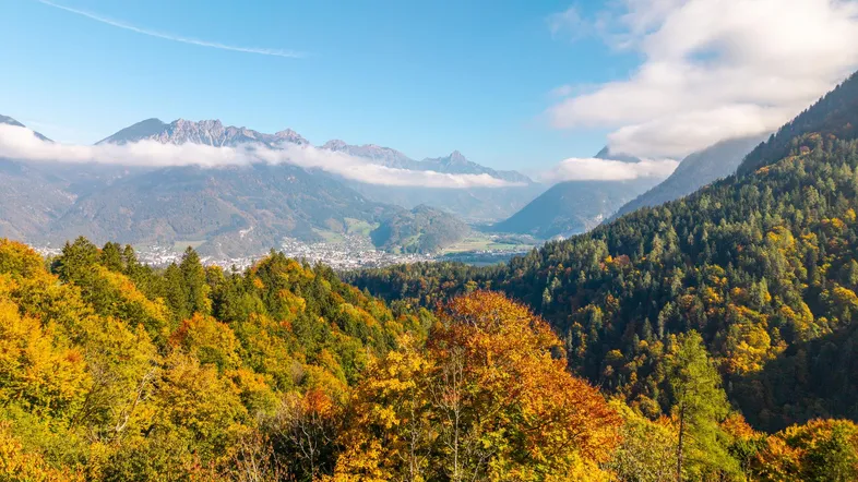 Malerische Herbstlandschaft mit weitem Blick über ein Tal und bewaldete Berge unter blauem Himmel.