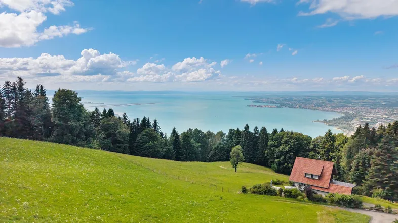 Malerisches Haus auf einem grünen Hügel mit weitem Blick über einen großen See und die umliegende Landschaft.