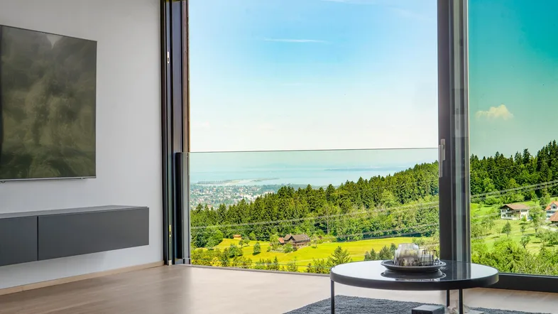 Helles Wohnzimmer mit großen Fenstern, die einen weiten Blick auf die Landschaft und den See bieten.