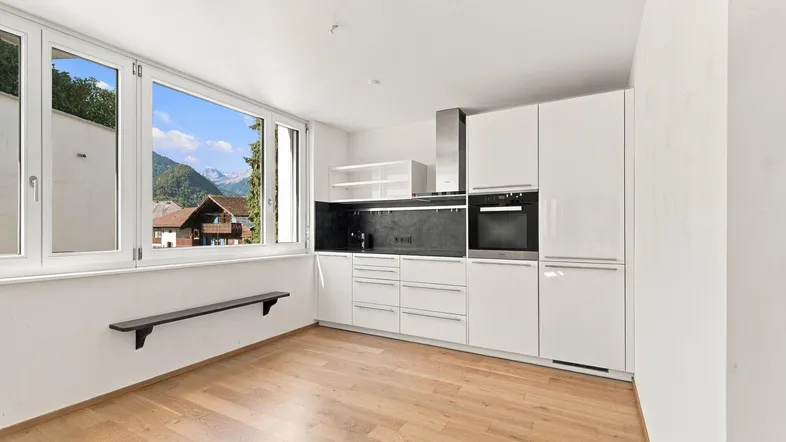 Moderne Einbauküche mit weißen Fronten, Bergblick und Holzboden.