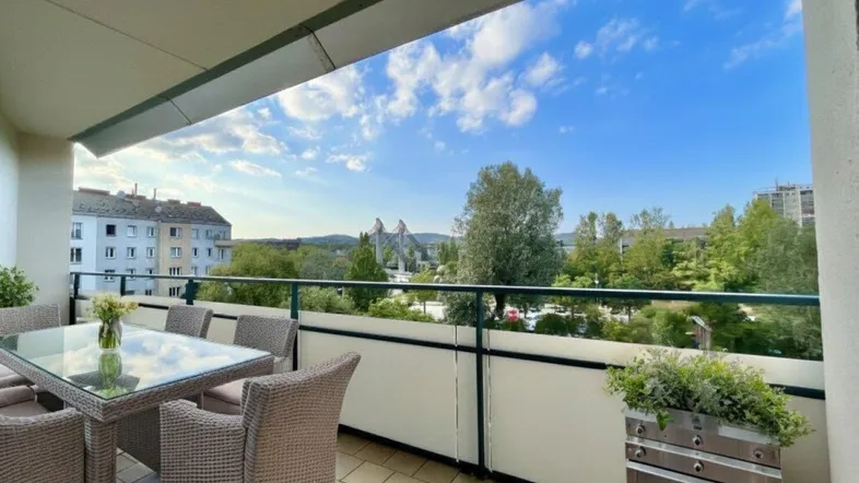 Geräumiger Balkon mit Esstisch, Stühlen und weitem Blick über die Stadt und Grünflächen.