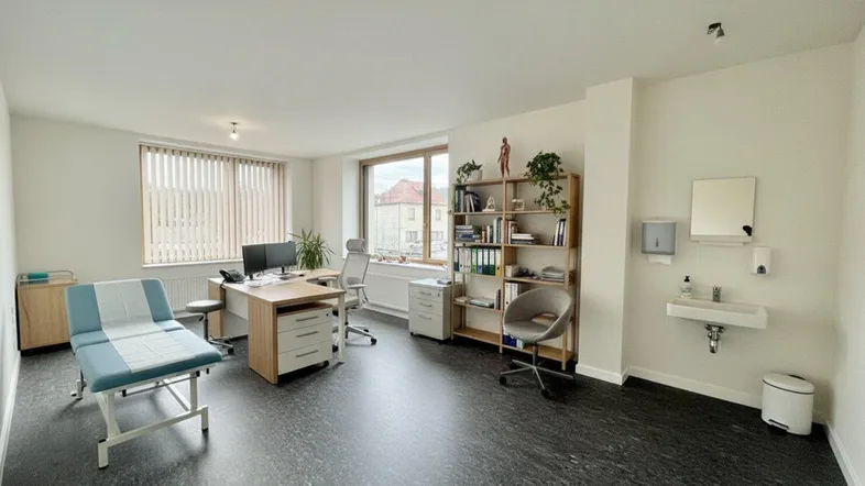 Geräumiges Büro mit dunklem Boden, großen Fenstern und einer Behandlungsliege, ideal für eine Praxis.