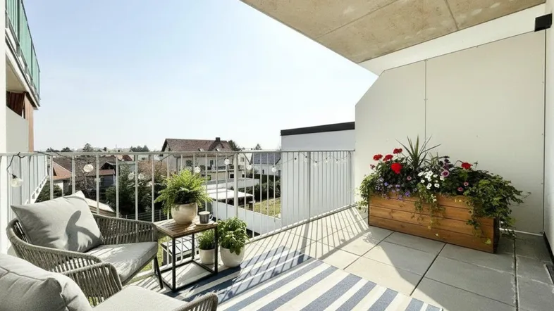 Heller Balkon mit gemütlicher Sitzgelegenheit, Pflanzen und weitem Blick über die Umgebung.