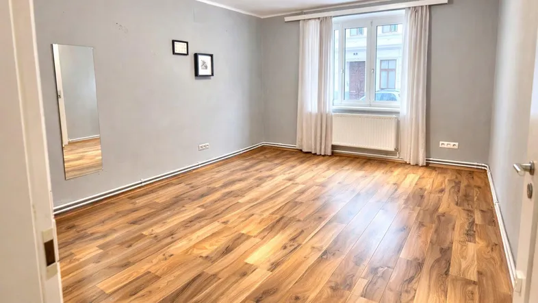 Helles, unmöbliertes Zimmer mit Laminatboden und grauen Wänden, ideal als Schlafzimmer.