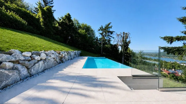 Infinity-Pool mit weitläufiger Terrasse, Steinmauer und atemberaubendem Blick auf die umliegende Landschaft und den See.